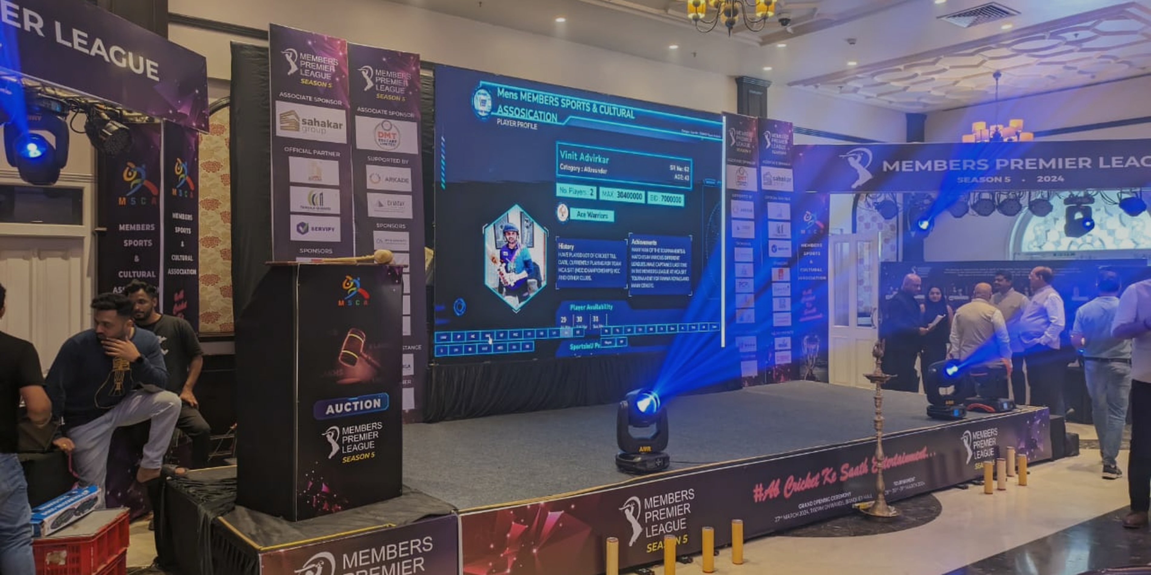 Stage set up for Cricket Premier League with spotlight and cricketer's name on the presentation screen, in side a banquet hall