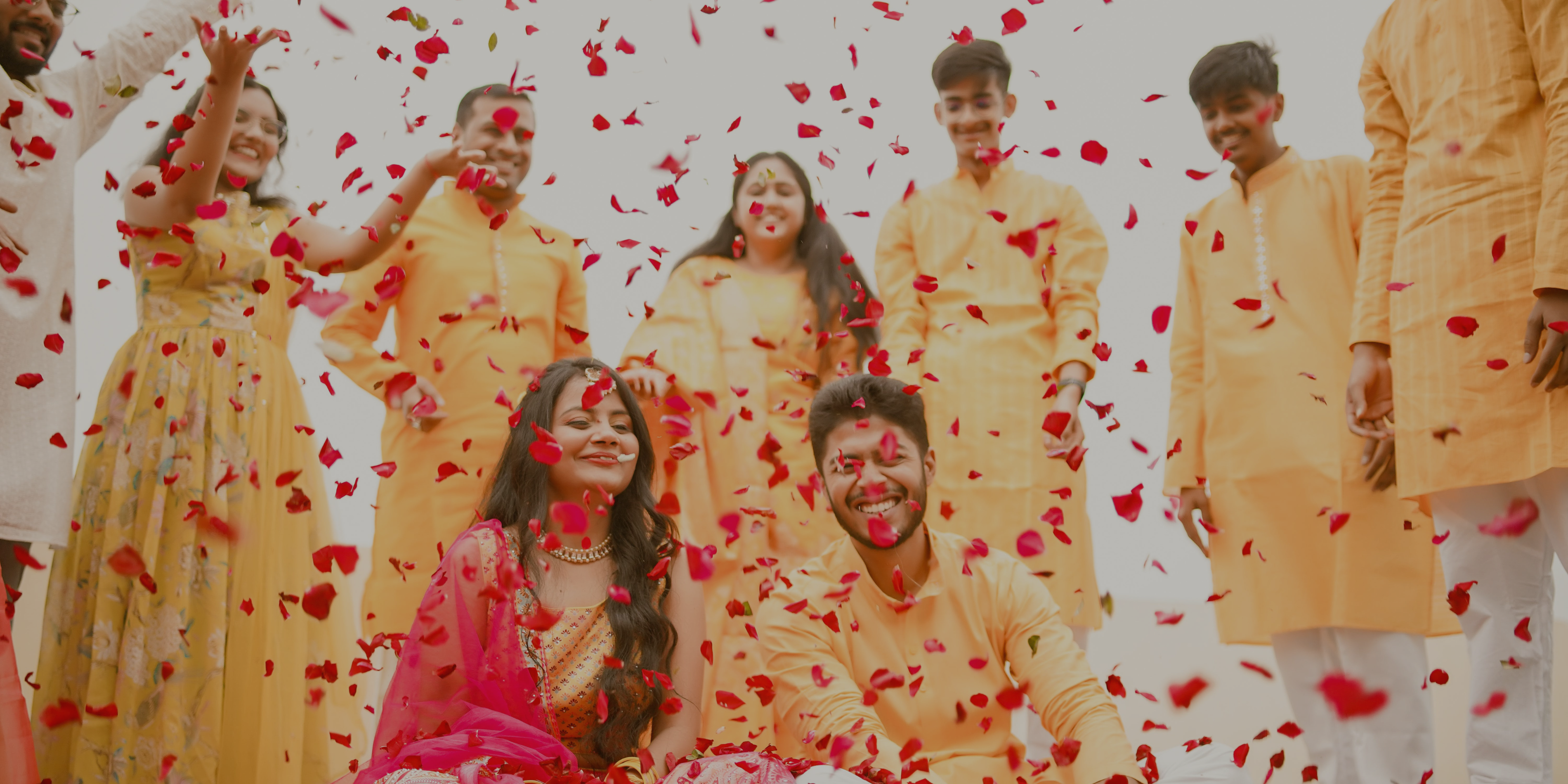 Bride and Groom Sitting in the center being showered with flowers by friends and family surrounding them on their haldi ceremony