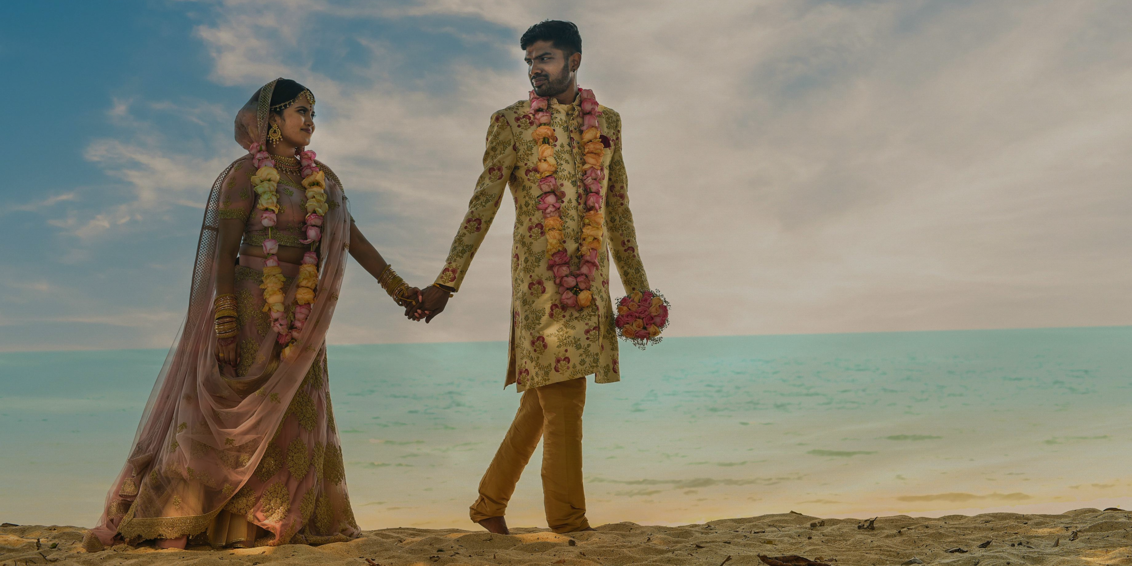 Couple walking on the beach with their wedding attire