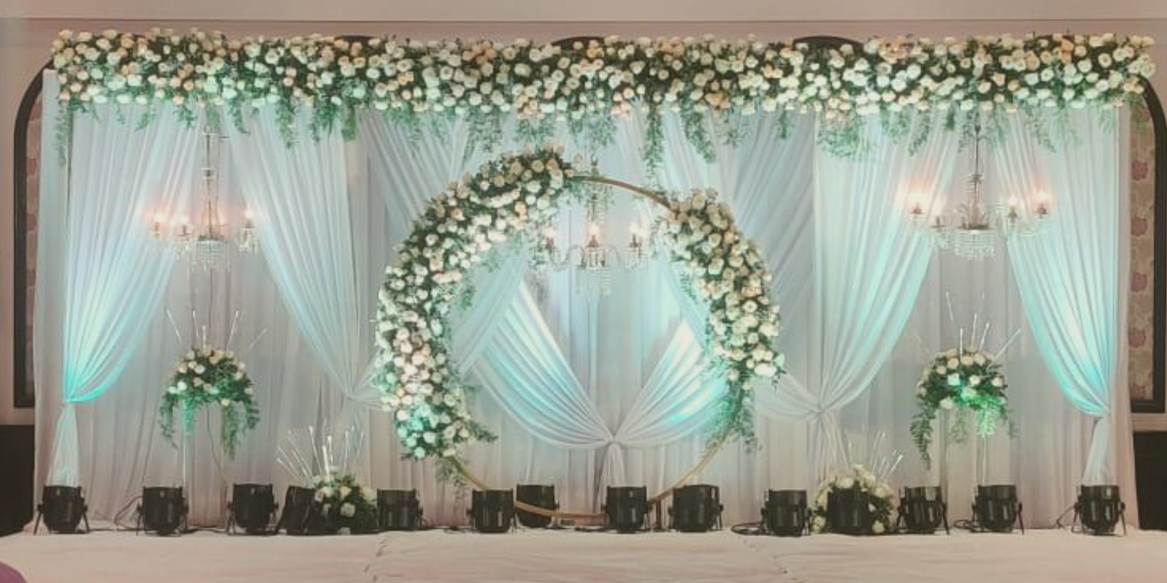 Reception stage decor with white back drop and white flowers decorated in a giant circle at the center